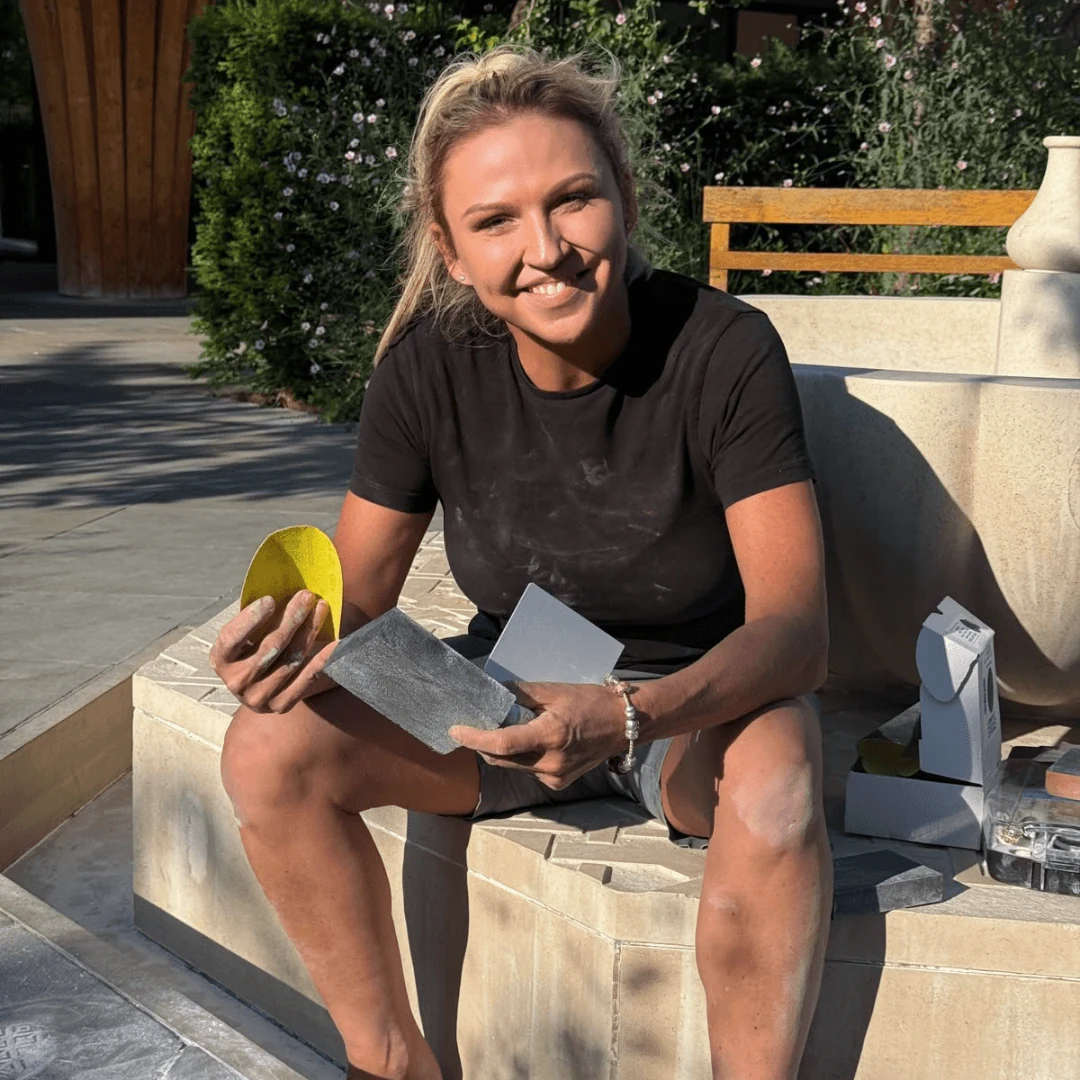 Adele, founder of Surface Artists, sitting on restored stonework with colour-matching tools
