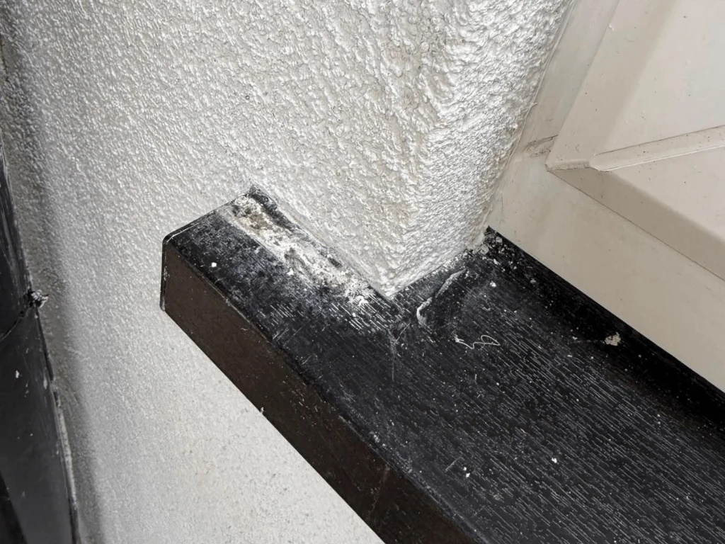 Before: damaged black uPVC window sill at the corner of a textured wall, with peeling finish and scratches
