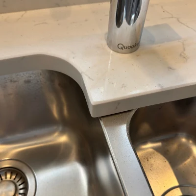 Stone worktop corner beside a kitchen sink after repair, with the chip restored